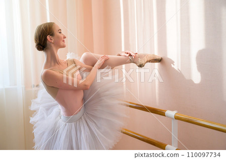 Beautiful graceful ballerina is practicing in the hall against the background of a window. Slender woman in tutu and pointe shoes in a dance class. 110097734