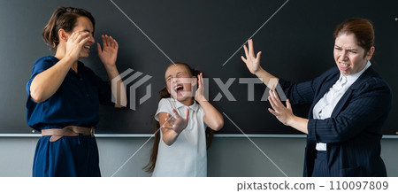 The female teacher screams at the schoolgirl and her mother standing at the blackboard. The female teacher screams at the schoolgirl and her mother standing at the blackboard. 110097809