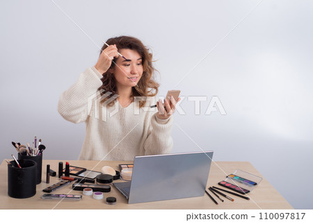 Young caucasian woman records video of online makeup training on a smartphone. Video blogger girl applies eye shadow Young caucasian woman records video of online makeup training on a smartphone. Video blogger girl applies eye shadow 110097817