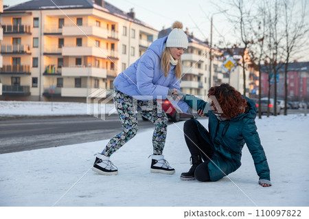 The girl supports her friend by the hand so she can get up. 110097822