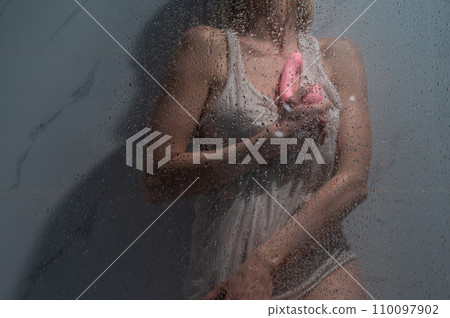 A woman in a white tank top stands in the shower and holds a curved pink sex toy.  110097902