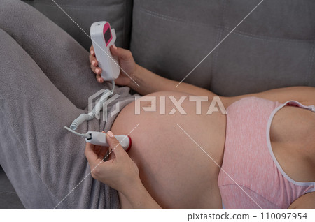 Close-up of a pregnant woman's belly using a home doppler. Blank screen. Close-up of a pregnant woman's belly using a home doppler. Blank screen. 110097954