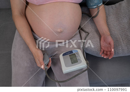Close-up of the belly of a pregnant woman measuring blood pressure with a tonometer. Hypotension.  110097991