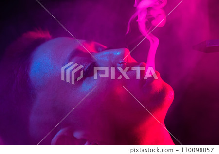 Close up portrait of asian woman with short hair smoking in neon light. Close up portrait of asian woman with short hair smoking in neon light. 110098057