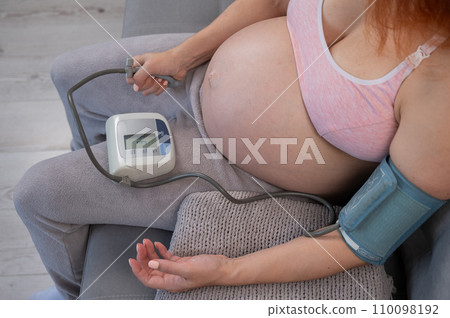 Close-up of the belly of a pregnant woman measuring blood pressure with a tonometer. Hypotension.  110098192