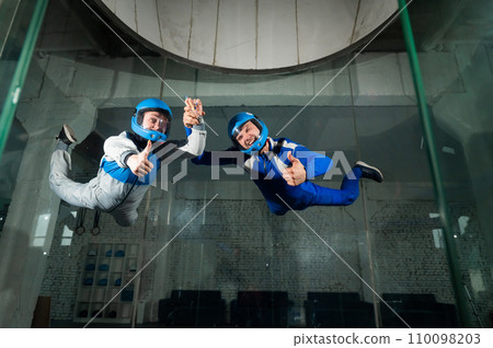 A man and a woman enjoy a joint flight in a wind tunnel and give a thumbs up. Free fall simulator. A man and a woman enjoy a joint flight in a wind tunnel and give a thumbs up. Free fall simulator. 110098203