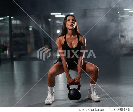 Caucasian woman squats with kettlebell in the gym.  110098476