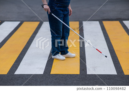 Close-up of the legs of a blind woman crossing the road at a crosswalk with a cane. Close-up of the legs of a blind woman crossing the road at a crosswalk with a cane. 110098482