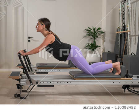 A pregnant woman does a plank on a reformer machine. Perinatal yoga. 110098488