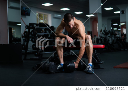 Muscular shirtless man sitting on a bench and lifting a dumbbell. Muscular shirtless man sitting on a bench and lifting a dumbbell. 110098521