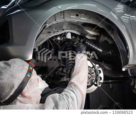 An auto mechanic applies anti-corrosion mastic to the underbody of a car. 110098523