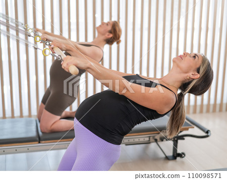 Two pregnant women do Pilates exercises on a reformer. Two pregnant women do Pilates exercises on a reformer. 110098571