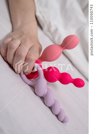 Woman holding three different anal beads while lying in bed.  110098743