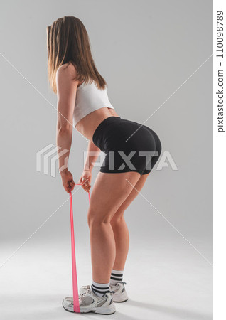 Caucasian woman doing exercises with fitness elastic band on white background. Vertical photo. Caucasian woman doing exercises with fitness elastic band on white background. Vertical photo. 110098789
