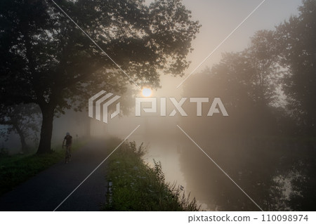 Cyclist on a Misty Riverside Journey at Dawn 110098974