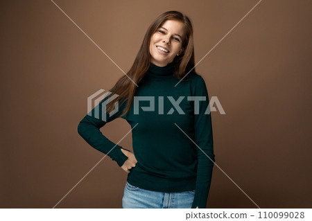 Portrait of a slender smiling European woman with brown hair on a brown background with copy space 110099028
