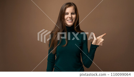 Confident young Caucasian woman with long brown hair points with her hand towards an advertisement Confident young Caucasian woman with long brown hair points with her hand towards an advertisement 110099064