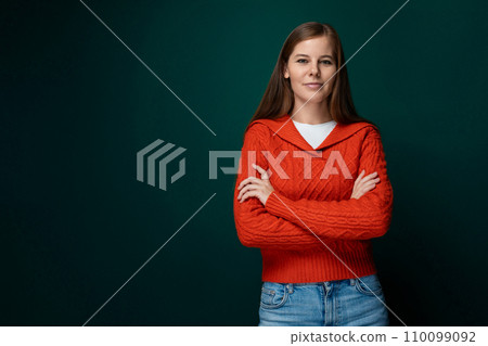 Well-groomed 30 year old woman with brown hair wears a red knitted sweater on a green background 110099092