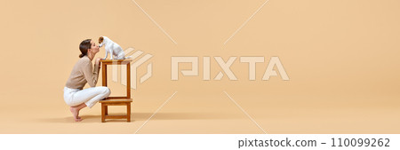 Banner. Happy woman playing with cute Jack Russell Terrier against beige studio background with negative space to insert text. Banner. Happy woman playing with cute Jack Russell Terrier against beige studio background with negative space to insert text. 110099262