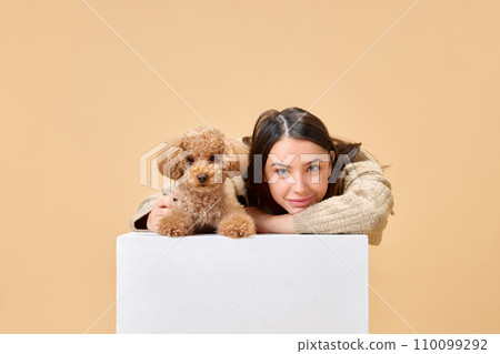Portrait of young and smiling girl, happy owner of little purebred dog with cute Poodle with kind and playful eyes against beige background. 110099292