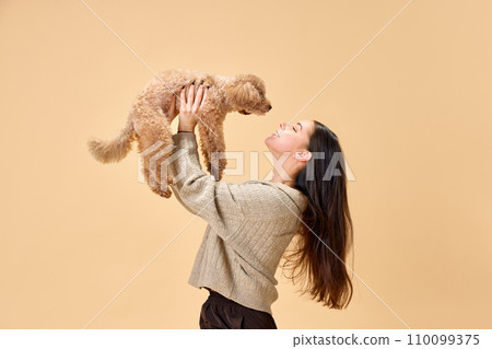 One beautiful young girl lovely looking at her cute pet with love and playing with her against beige studio background. Concept of pet lovers 110099375