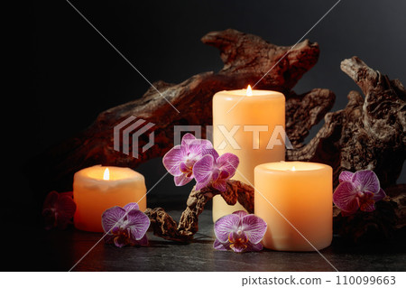 Orchid flowers, burning candles, and old wooden snags on a black background. Orchid flowers, burning candles, and old wooden snags on a black background. 110099663