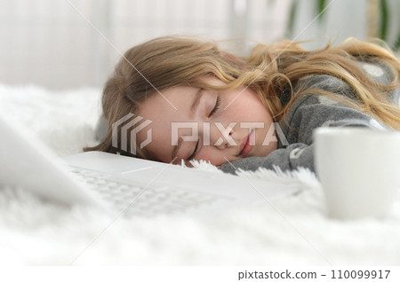 Little girl sleeping in her bed in front of the laptop 110099917