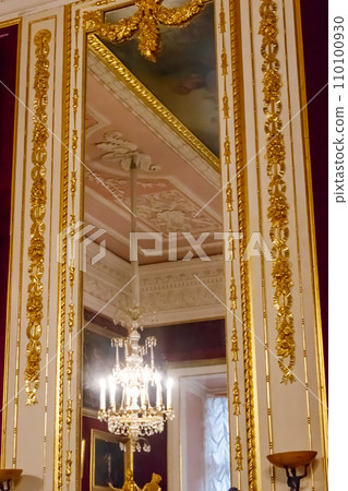 Large mirror in gilded ornate frame on a wall in luxurious room 110100930
