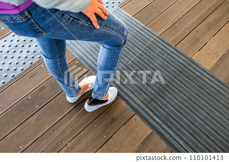 Female legs in denim jeans pants and light summer sneakers standing on wooden floow. Female legs in denim jeans pants and light summer sneakers standing on wooden floow. 110101413