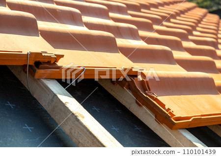 Closeup of metal montage anchor for installation of yellow ceramic roofing tiles mounted on wooden boards covering residential building roof under construction. Closeup of metal montage anchor for installation of yellow ceramic roofing tiles mounted on wooden boards covering residential building roof under construction. 110101439