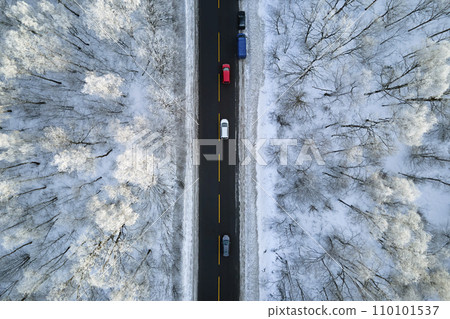 Aerial view of winter landscape with snow covered woods and black asphalt forest road on cold wintry day 110101537
