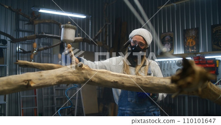 Creative female carpenter sprays liquid or wood varnish on tree branch Creative female carpenter sprays liquid or wood varnish on tree branch 110101647