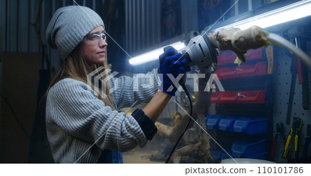 Female carpenter sands tree branch using sanding machine Female carpenter sands tree branch using sanding machine 110101786