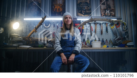 Female carpenter, artisan smiles and looks at camera sitting in workshop 110101796