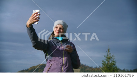 Female hiker takes selfie during trip or trek in mountains using phone 110101799