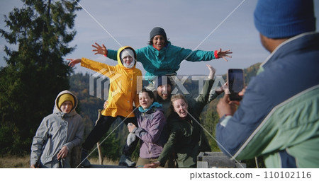 Diverse tourists smile and wave at camera standing against mountains landscape Diverse tourists smile and wave at camera standing against mountains landscape 110102116
