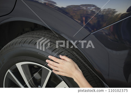 Female driver hands inspecting wheel tire of her new car. Vehicle safety concept 110102375