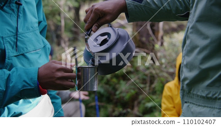 Tourist keeps metal cup in hand, other traveler pours hot water Tourist keeps metal cup in hand, other traveler pours hot water 110102407
