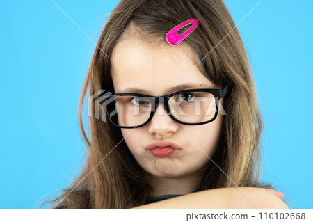 Close up portrait of angry displeased child school girl wearing looking glasses isolated on blue background. 110102668