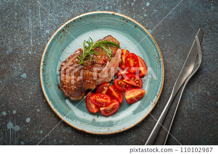 Delicious roasted duck breast fillet with golden crispy skin, with pepper and rosemary, top view on ceramic blue plate served with cherry tomatoes salad, rustic concrete rustic background Delicious roasted duck breast fillet with golden crispy skin, with pepper and rosemary, top view on ceramic blue plate served with cherry tomatoes salad, rustic concrete rustic background 110102987