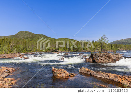 Namsen River with large stones and trees on a sunny day, bordered by dense forests 110103413
