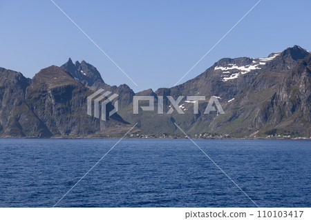 Tranquil Northern Sea with Moskenes' mountain ridge and harbor town in Lofoten 110103417