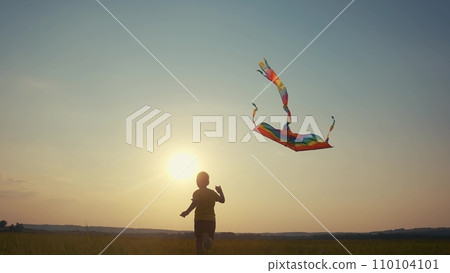 boy running with a kite. happy family kid dream concept. boy son running with his back sunset silhouette playing with a kite glare of the sun. happy child lifestyle playing with a kite with 110104101