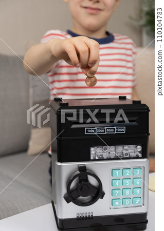 A little boy puts a coin into a safe piggy bank. Financial literacy for children. A little boy puts a coin into a safe piggy bank. Financial literacy for children. 110104783