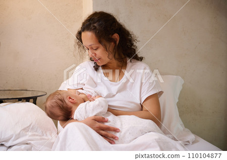 Newborn baby boy sucking milk from mothers breast. Confident portrait of a beautiful woman, young loving mom while breastfeeding baby in cozy home interior. Pregnancy and maternity leave lifestyle Newborn baby boy sucking milk from mothers breast. Confident portrait of a beautiful woman, young loving mom while breastfeeding baby in cozy home interior. Pregnancy and maternity leave lifestyle 110104877