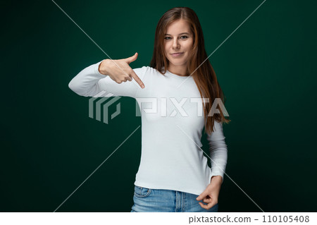 A cheerful woman dressed in a white turtleneck points her finger at an advertisement 110105408