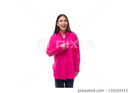 smart young brunette woman in a bright pink shirt points her finger at the space for advertising on 110105415
