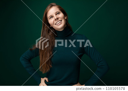 Smiling cheerful young woman with brown hair wearing a green turtleneck 110105578