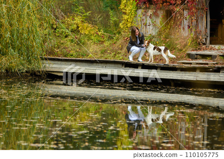 Young beautiful girl petting a dog near a lake in an autumn park 110105775