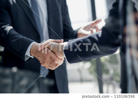executives shaking hands in front of their manager and a colleague 110106398